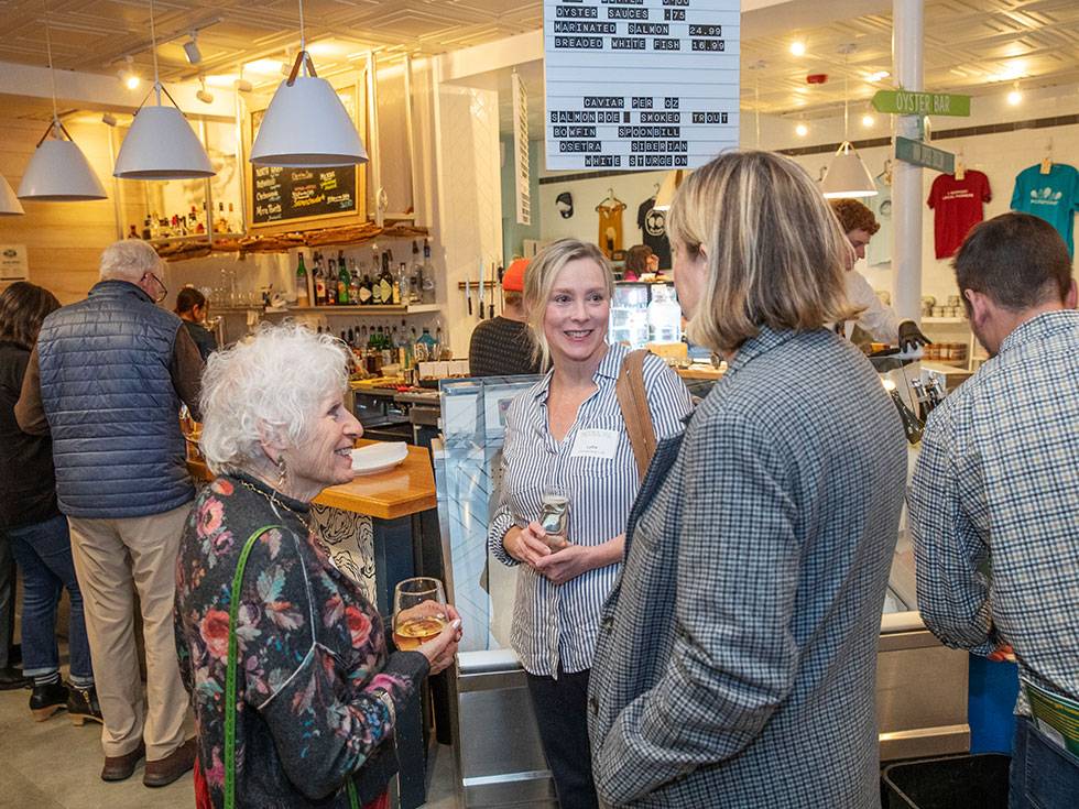 Three alums converse in a circle with a lively restaurant scene in the background