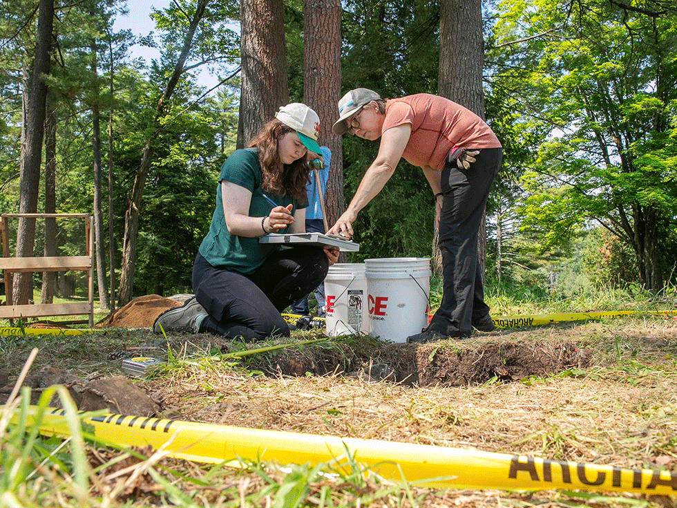 Skidmore College student Lily Whelden ’25 works to excavate artifacts from the site of a Revolutionary War-era smallpox hospital in Lake George Battlefield Park with Professor of Anthropology Siobhan Hart