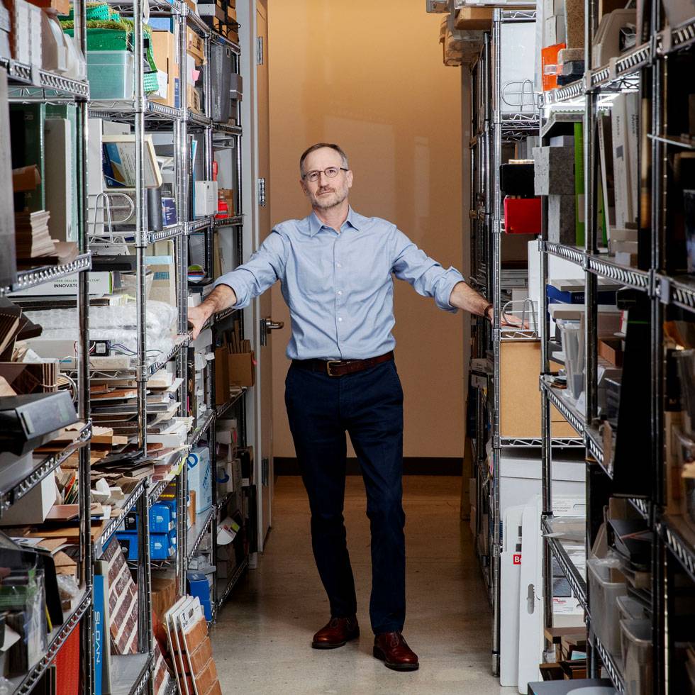 David Levine stands in an aisle of book cases, with his arms resting on either side.
