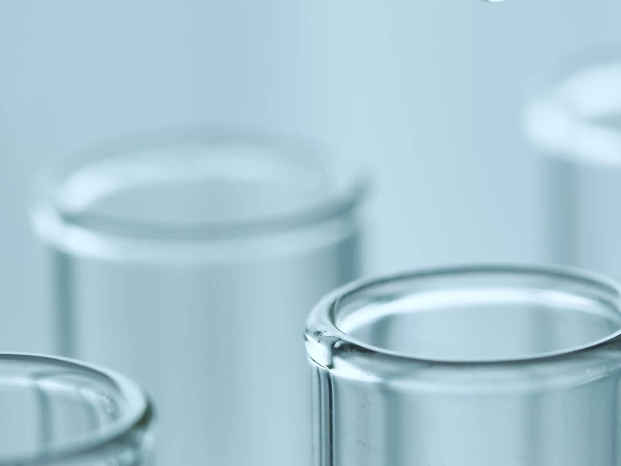 Glass science beakers sit on a table with a grey background, filled partially with clear liquid.