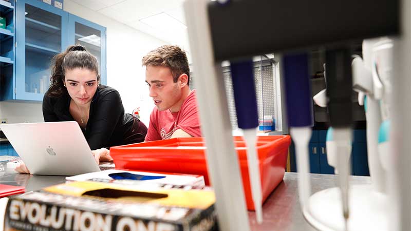 two students looking over a computer with labe equipment in front of them