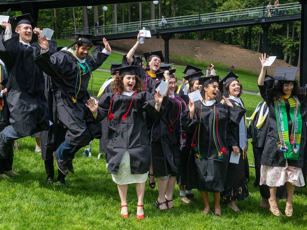 A group of graduates celebrate in their regalia by jumping up in SPAC's green lawn