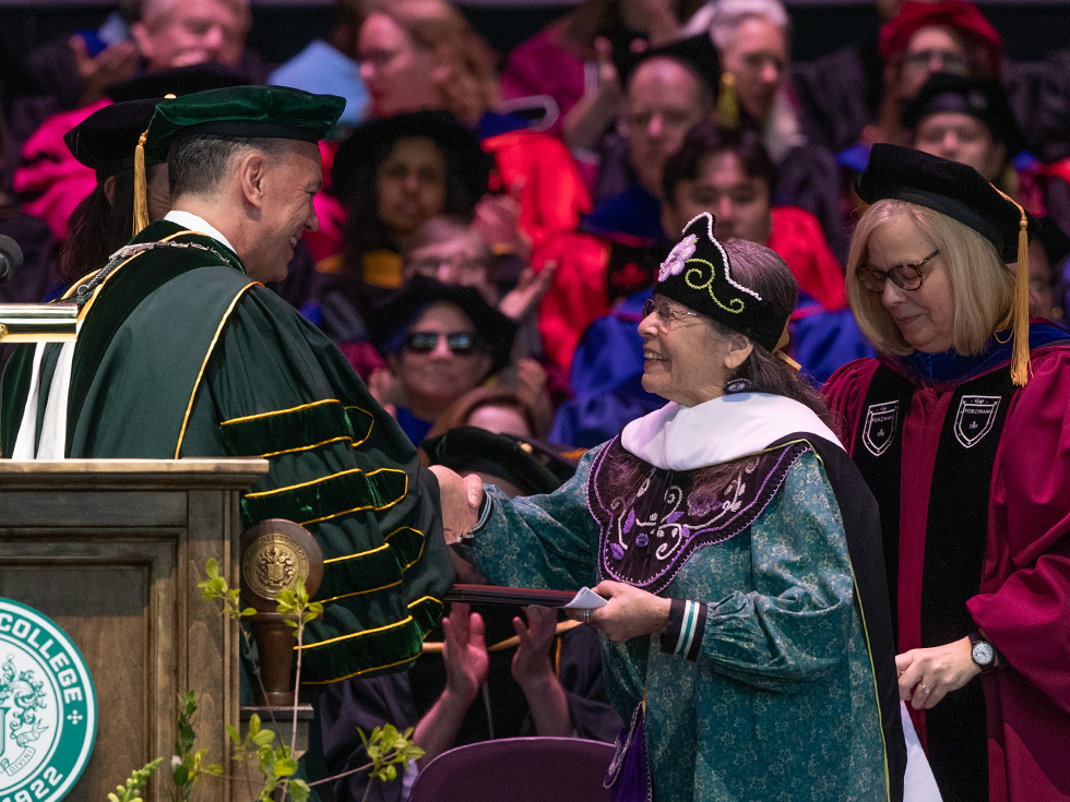 Speaker Kay Olan in decorative Mohawk Nation academic regalia and a beaded hat addresses the Skidmore commencement audience from the podium.