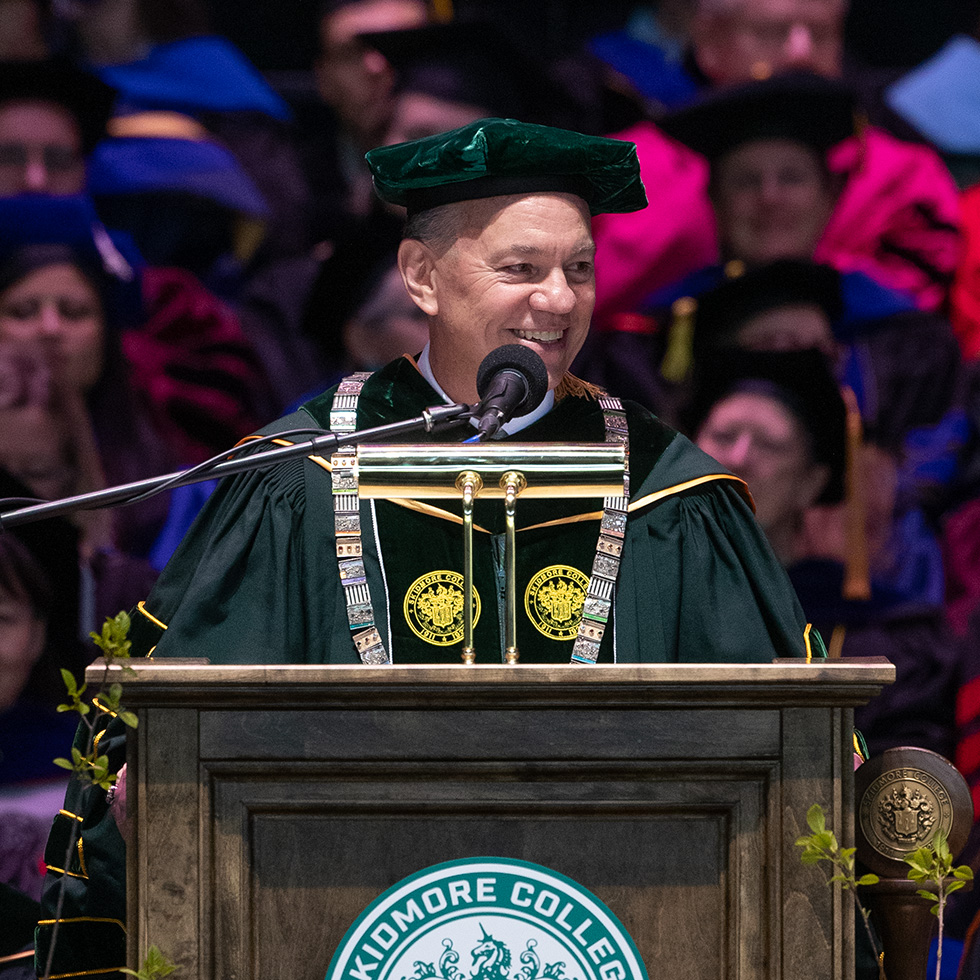 Marc C. Conner in green academic regalia addresses the audience from a podium during Skidmore’s commencement ceremony.