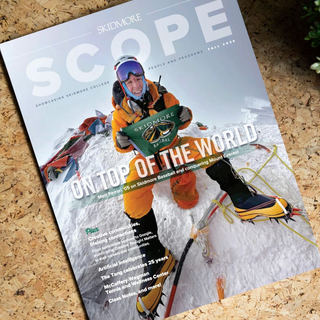 Cover of Skidmore’s Fall 2025 SCOPE magazine featuring an alumnus in mountaineering gear kneeling on a snowy peak and holding a Skidmore Baseball banner, with the headline “On Top of the World.”