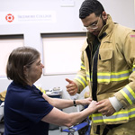 Denise L. Smith, director of the First Responder Health and Safety Laboratory at Skidmore, helps Marcus Jackson '18 put on firefighting gear during a recent research session.