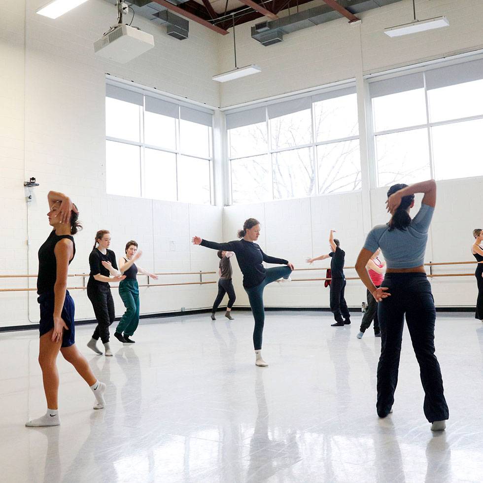Multiple Skidmore dancers warming up in Skidmore's dance performance space, with natural light beaming through back corner windows.