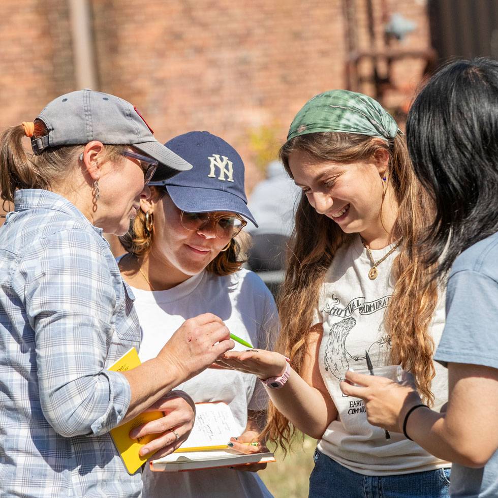 Three students and a professor examine a small object in one person’s hand during an outdoor field study.