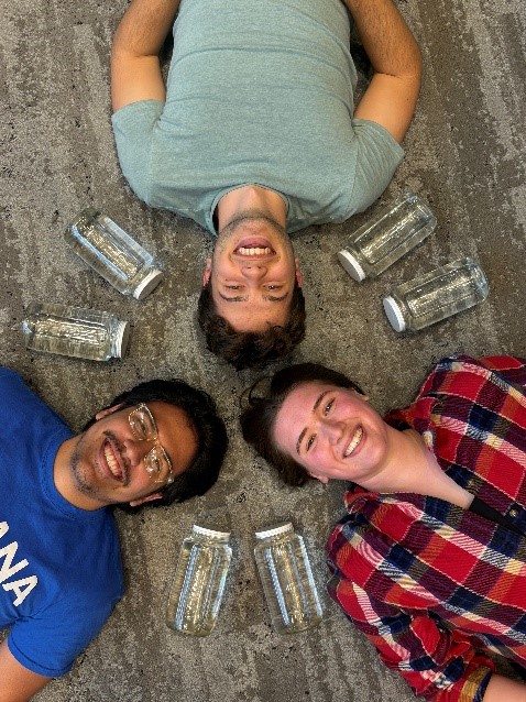 3 students laying on the floor looking up at the camera smiling
