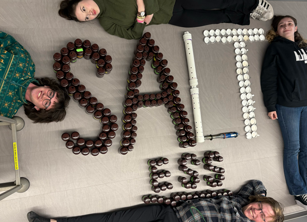 Students posing on the floor, around a sign that says "saltless"