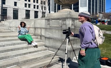 Students making a film on the steps of a large campus building