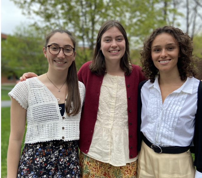 3 students standing outside, smiling.