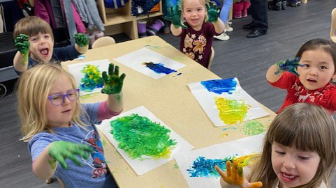 Kids sitting at table finger painting with yellow and blue paint