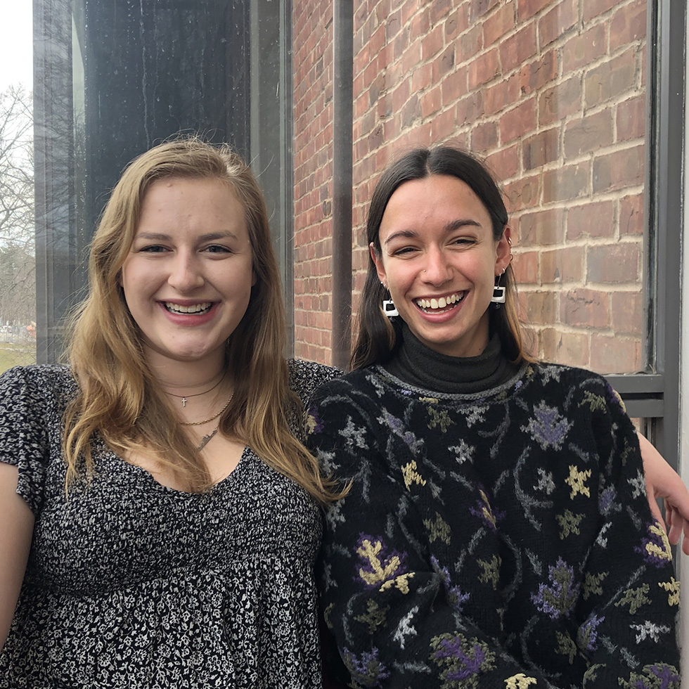 Two students stand together smiling.