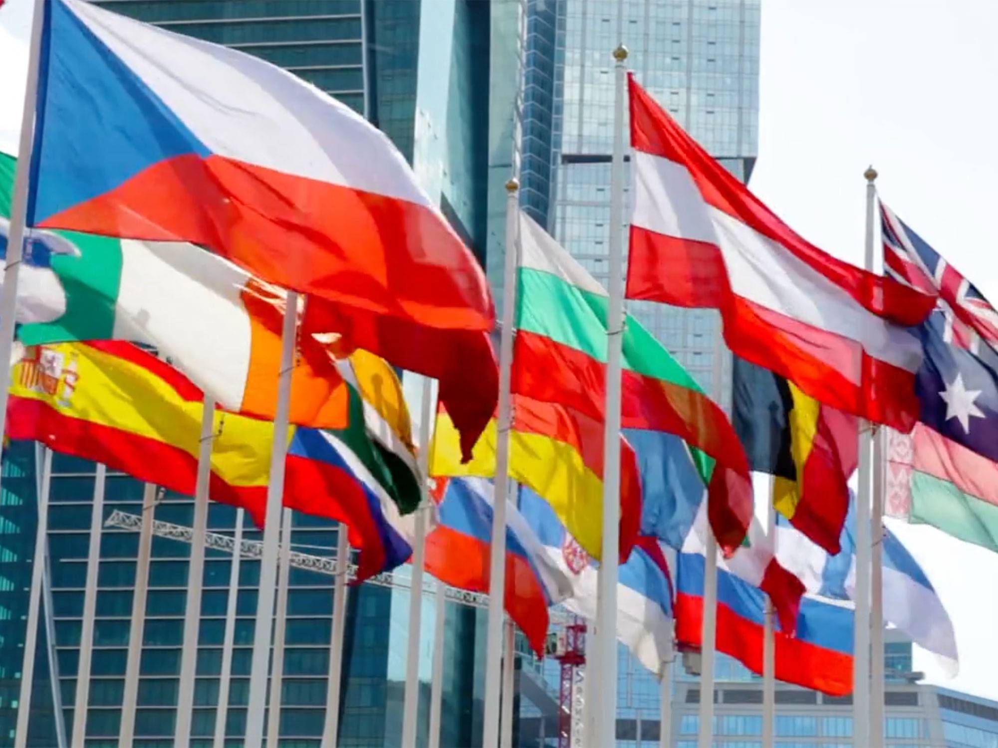 Various world flags blowing in the window with skyscrapers in the background.