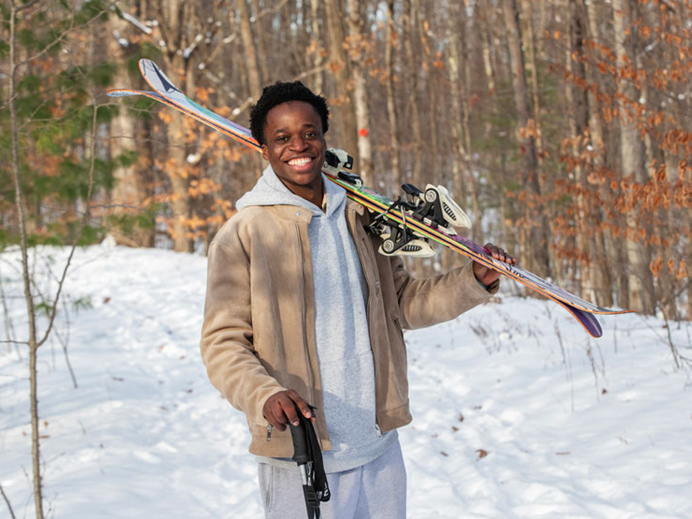 Suleiman Lailati stands in a snowy wooded area holding skis.