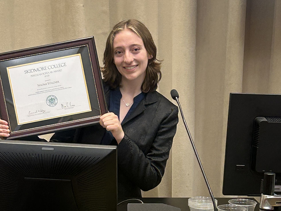 Student stands holding an award.