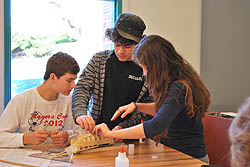 Three students take a turn assembling a model of Cook's HMS Endeavor.