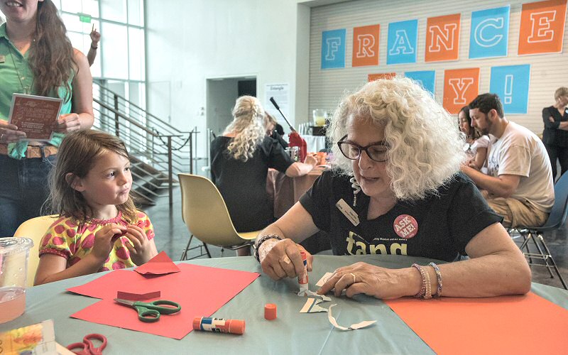 At the Build a Better World table, museum educator Ginger Ertz (at right) helps a youngster to fold, cut, glue and otherwise incorporate maps in creating a new artwork.