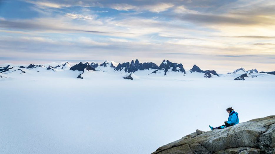 Student works in a sketch book while overlooking an ice field in Alaska