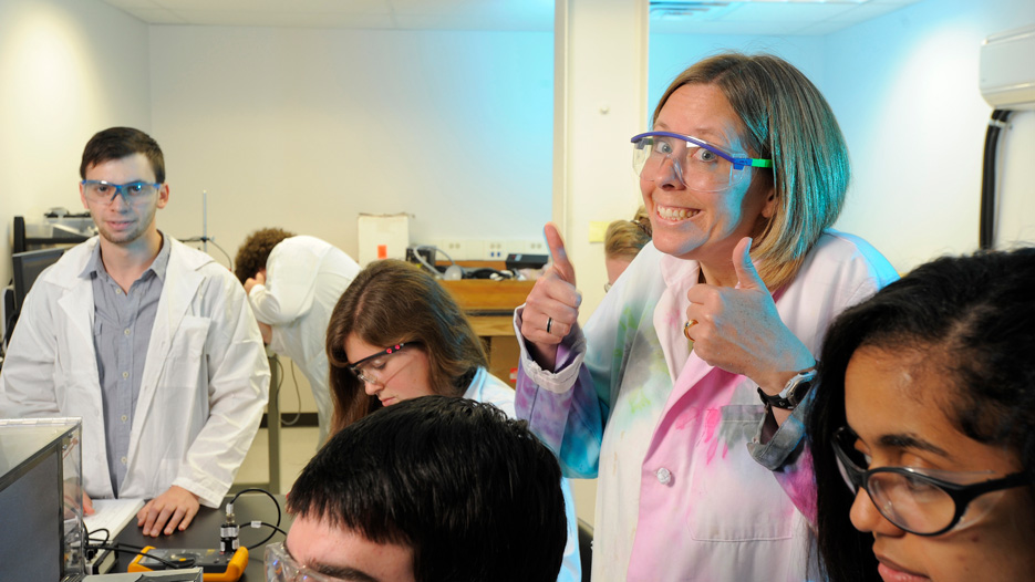 Kim Frederick, chemistry professor, gives two thumbs up in a laboratory