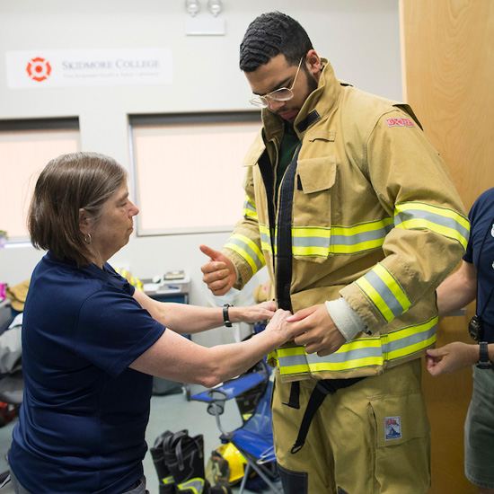 Denise+L.+Smith%2C+director+of+the+First+Responder+Health+and+Safety+Laboratory+at+Skidmore%2C+helps+Marcus+Jackson+%2718+put+on+firefighting+gear+during+a+recent+research+session.+