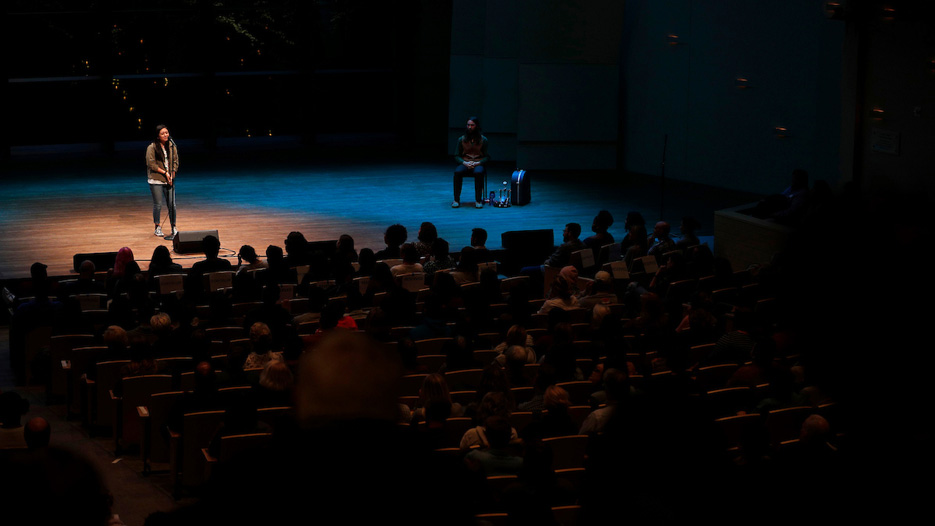 Female student on stage under a spotlight speaks into a microphone