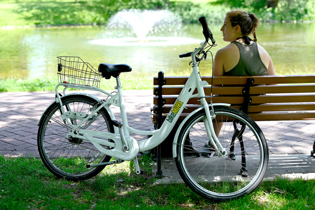 A college student sits by her bike in a public park