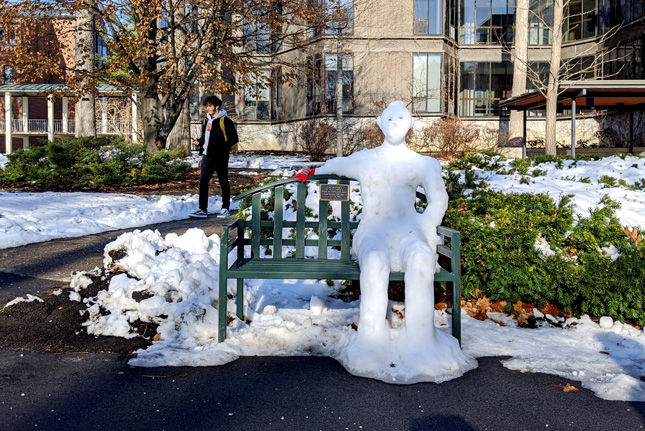 A snow scultpure of a person sitting on a bench