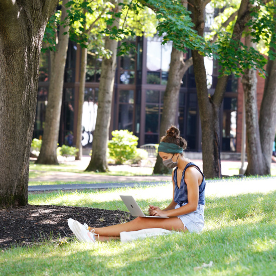 A+student+uses+her+laptop+in+the+shade.+