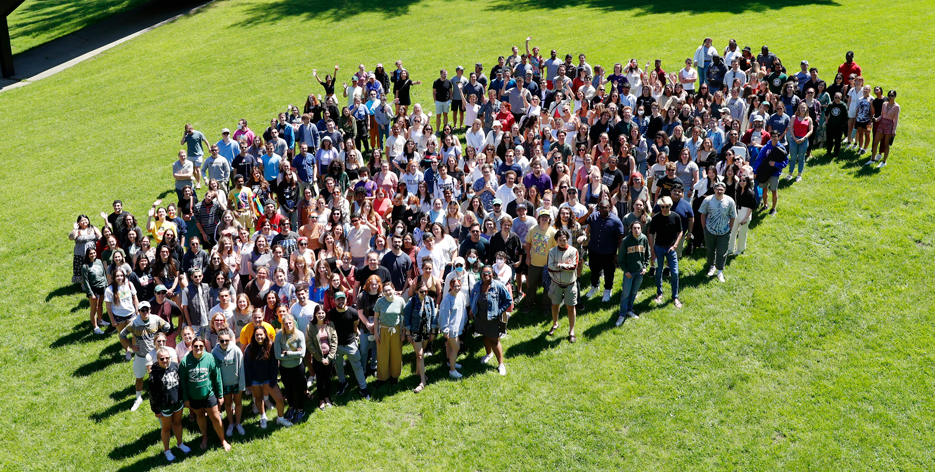 A crowd of over 500 college students stand in a grassy field