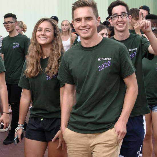 Three+college+students+in+matching+T-Shirts+that+say+%22Skidmore+2020%22+parade+into+a+ceremony+