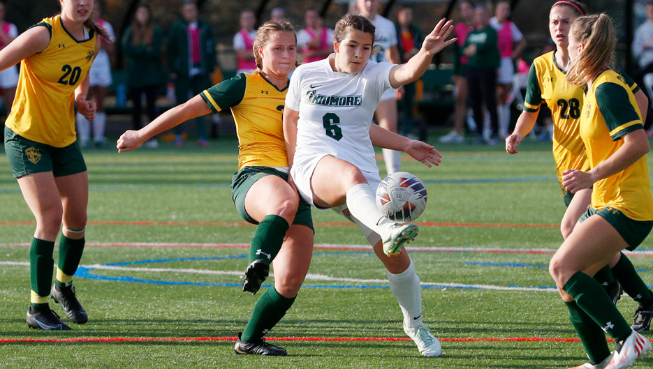 several women's soccer players compete for the ball, one is mid-kick