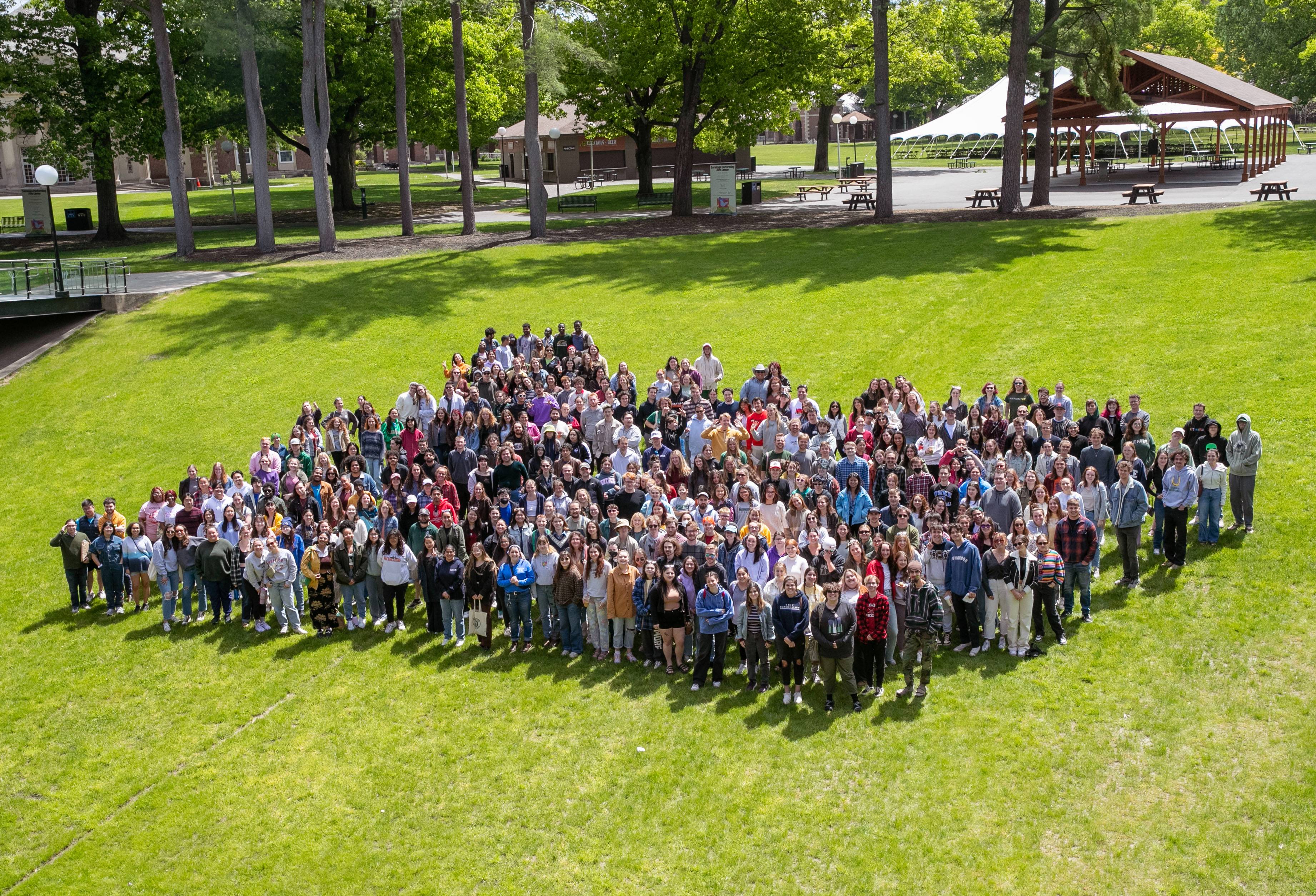 A crowd of college students stand in a grassy field