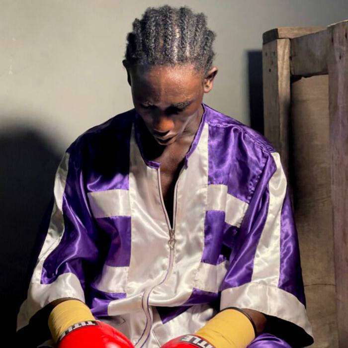 A boxer from Jamestown sits wearing his gloves, head down.