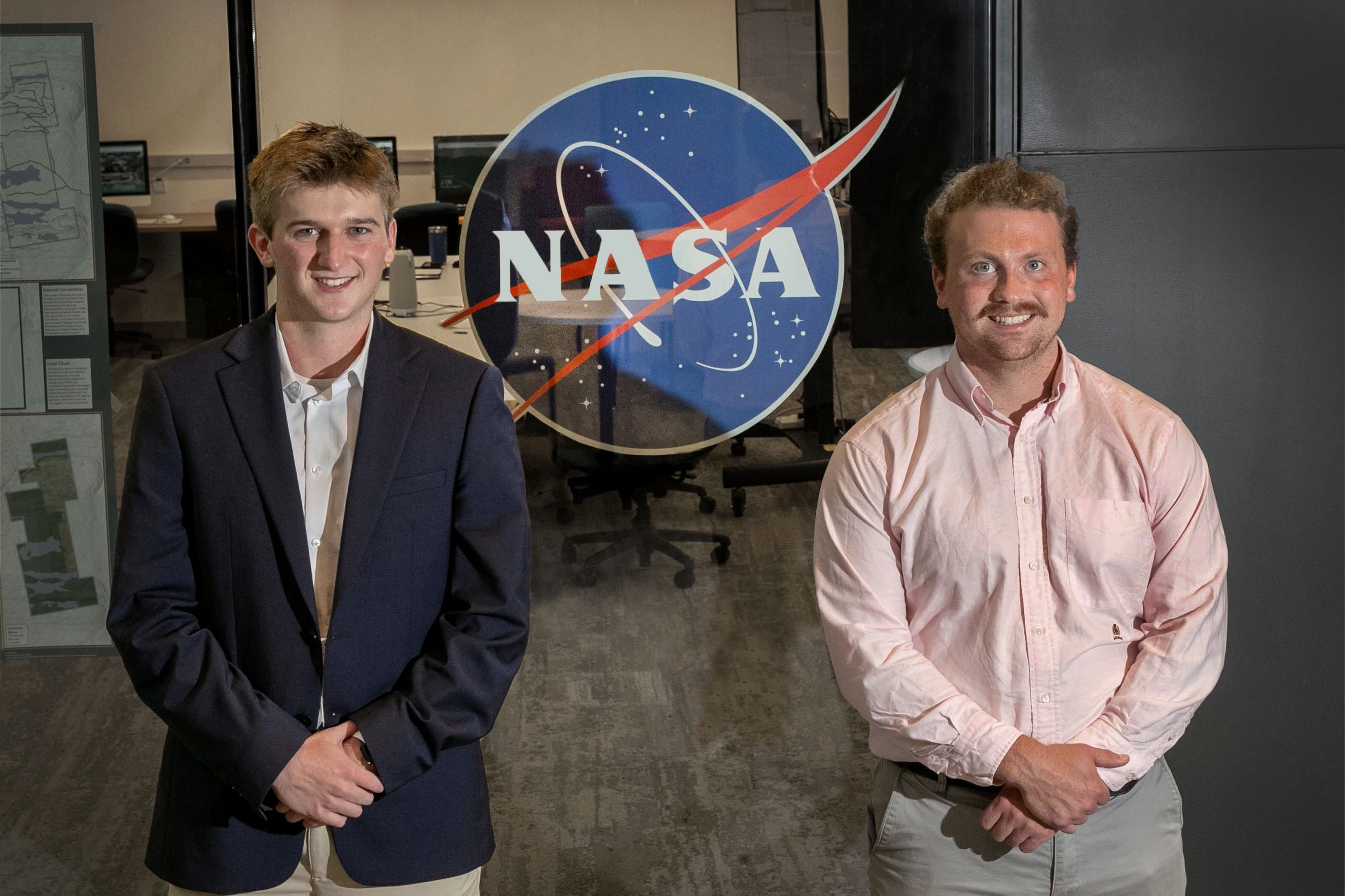Skidmore College students Sam Haas '24 and Oliver Wilson '23 stand in front of a NASA sign in the Billie Tisch Center for Integrated Sciences