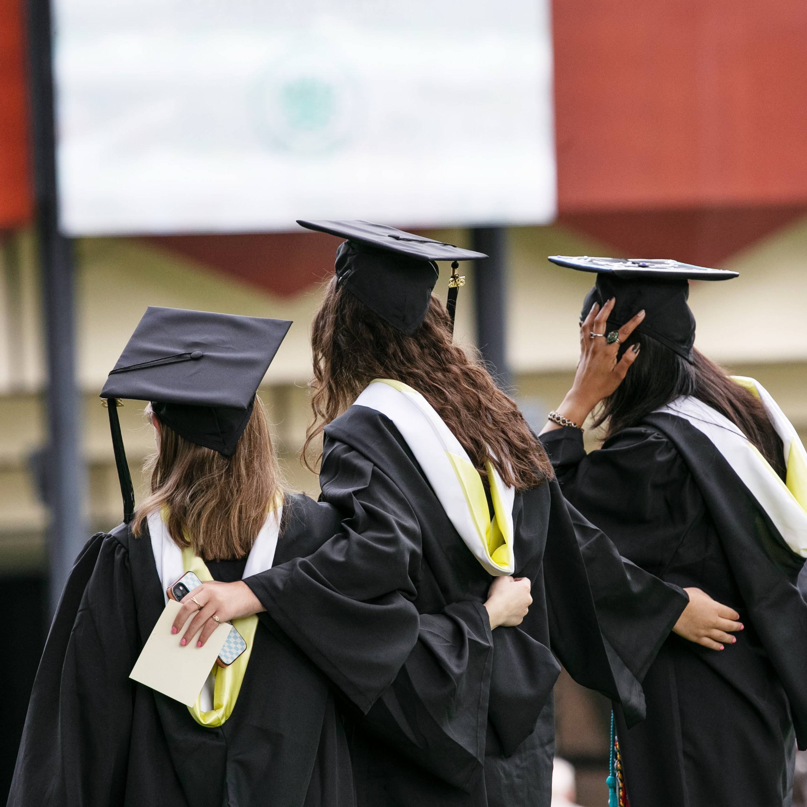 Three+Skidmore+graduates+face+away+from+the+camera+with+their+arms+around+each+other+during+2023+Commencement.+