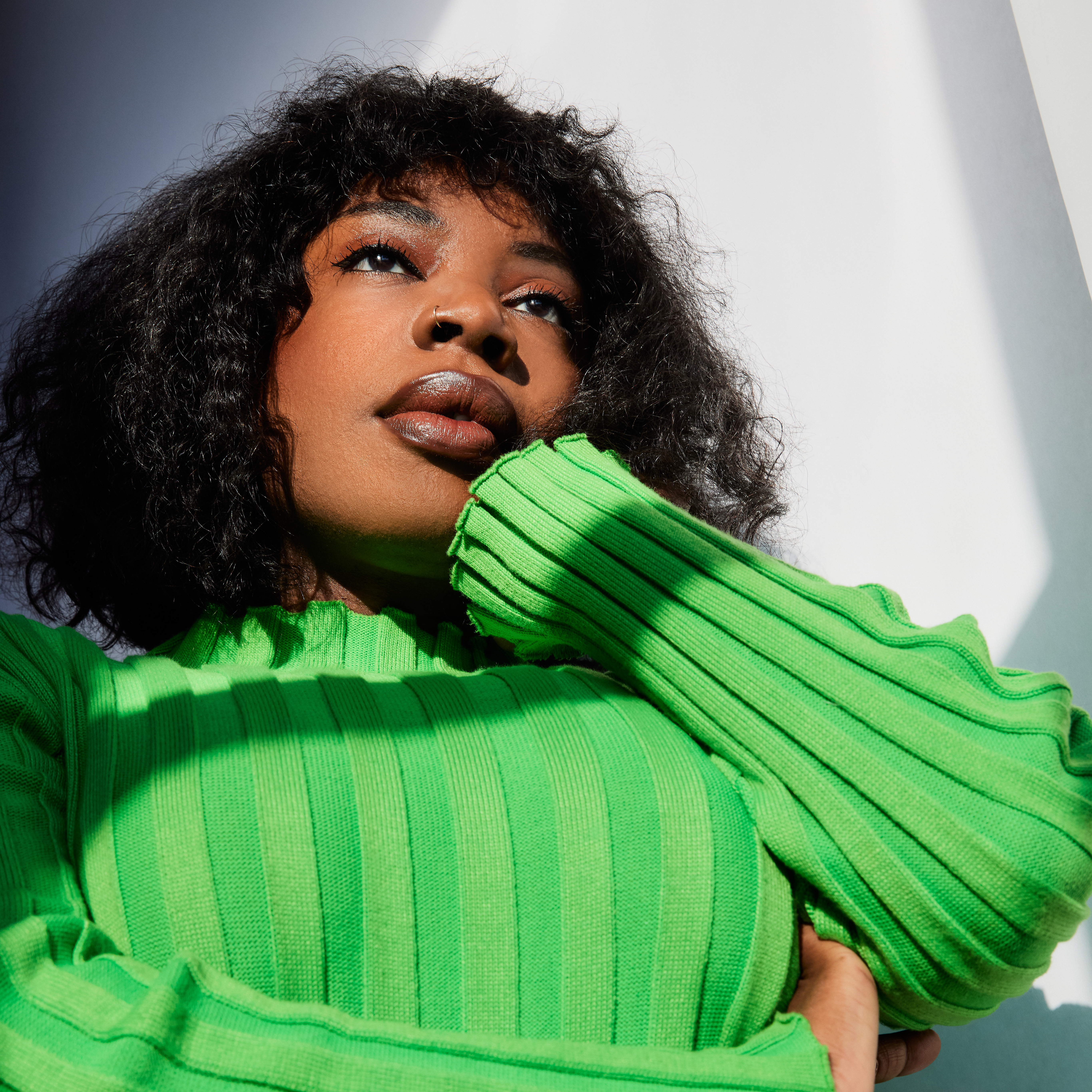 Melanie+Charles+gazes+offscreen%2C+head+resting+in+hand%2C+wearing+a+green+shirt