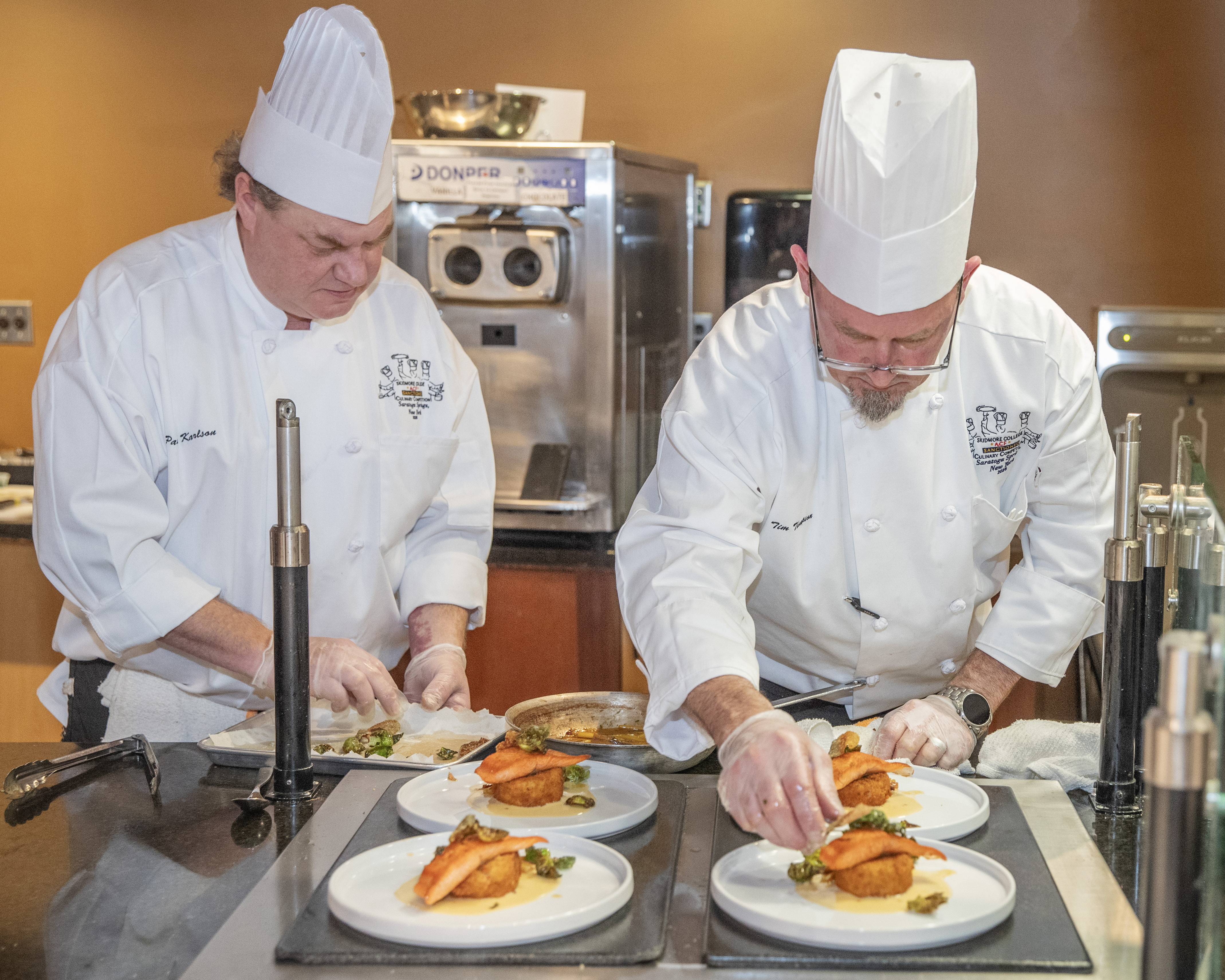 Senior Cook Paul Karlson and Production Manager Tim Thompson work together to plate the team's trout-based entrée.