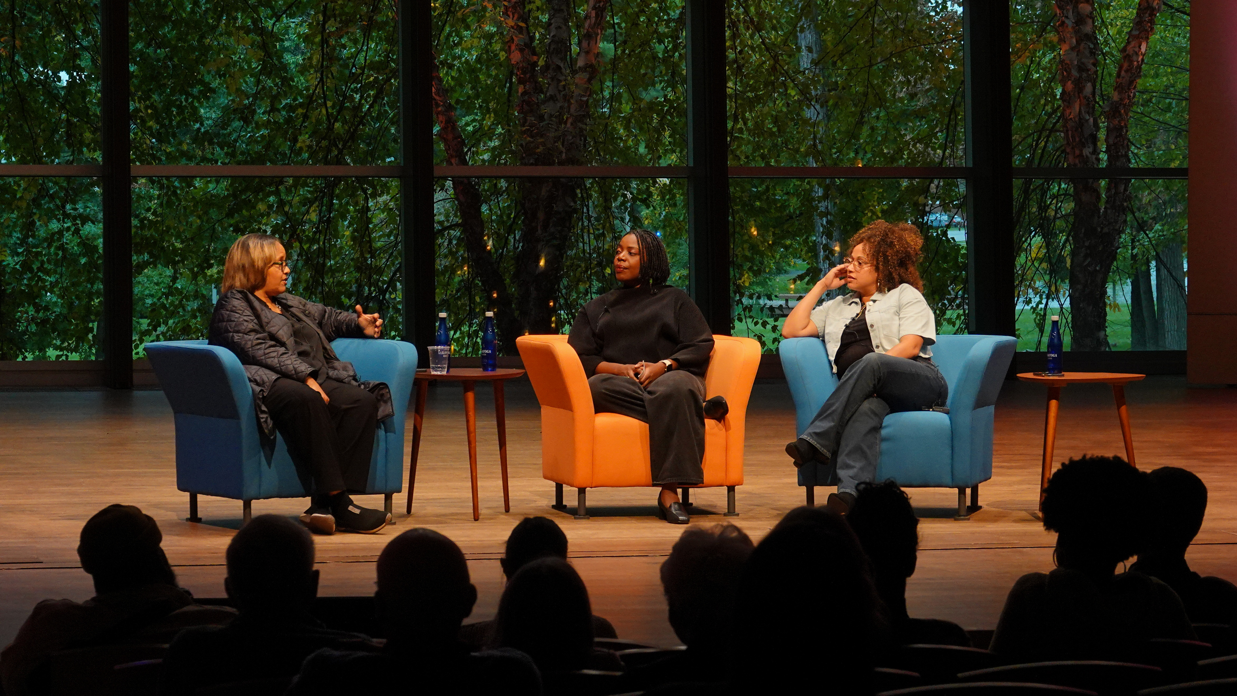Melanie Charles sits in an orange chair onstage at Zankel Music Center alongside Yunie Mojica and Terri Lyne Carrington, both in blue chairs.