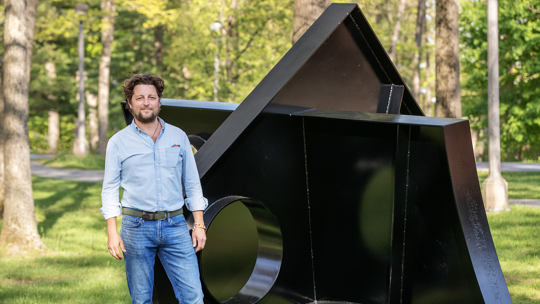 Fitzhugh Karol ’04 stands beside "Tingwon" on Skidmore's campus. He wears a blue shirt and blue jeans: He has his hands by his sides and is smiling.