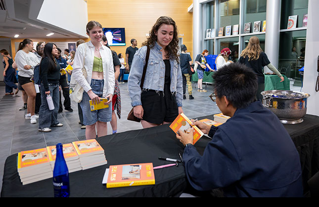 Students wait in line at a book signing with the author sitting at a table.