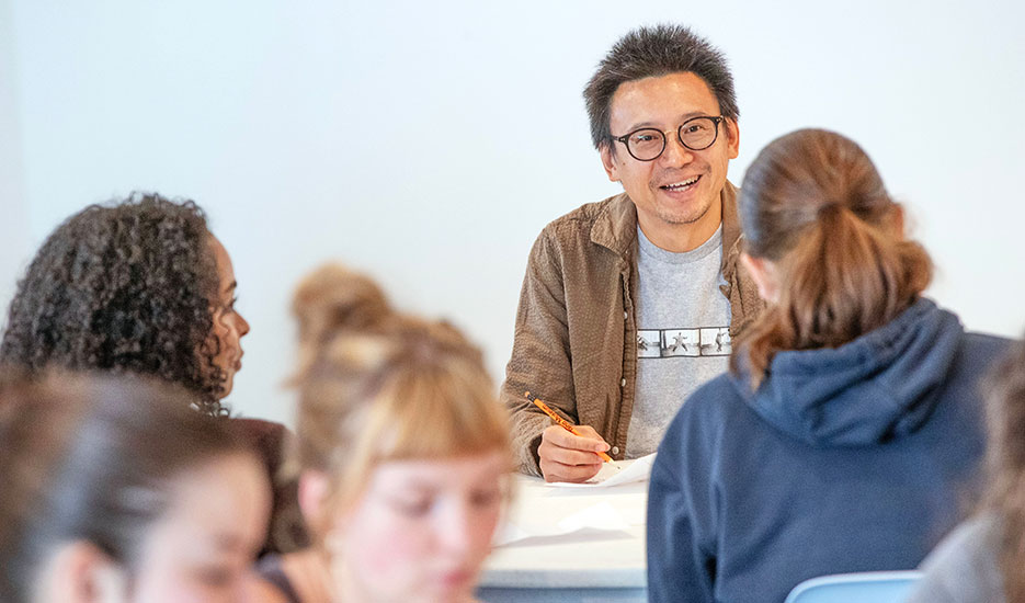 Author Hua Hsu sits at a table and speaks to Skidmore students.