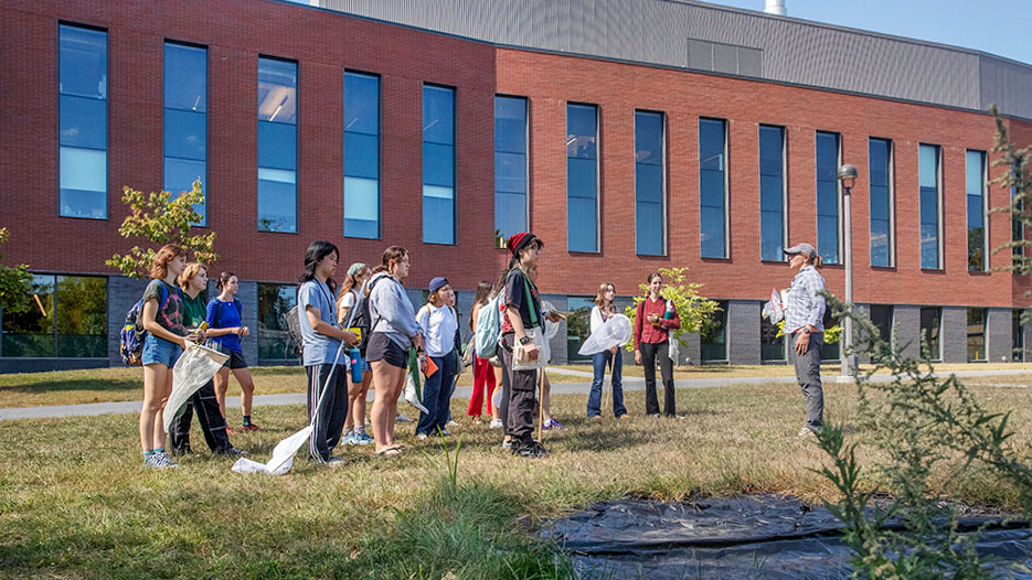 A group of students and a professor standing at the future site of their pollinator garden. 