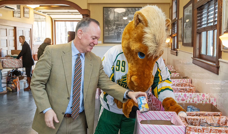 Skidmore College President Marc Conner and the college mascot, Skids, place donated items into collection bins. 
