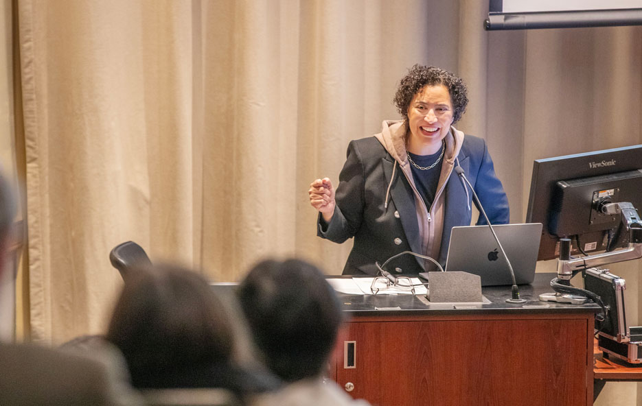 Meredith Broussard stands at a podium, smiling and gesturing with her hands as she speaks to an audience.