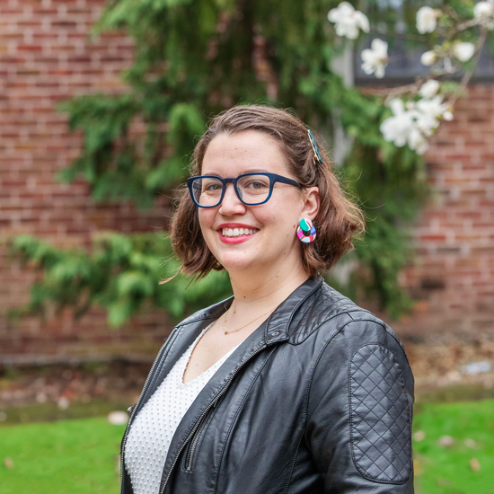 Sarah+Faude+stands+outside+on+the+Skidmore+campus%2C+in+front+of+a+brick+building+and+greenery
