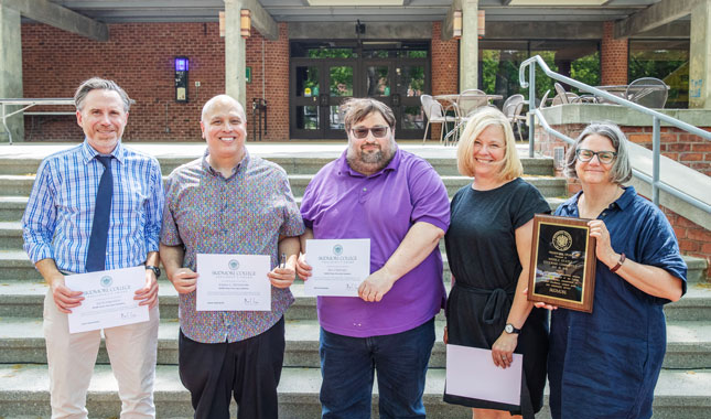 Five employees stand side by side smiling while accepting a team award.