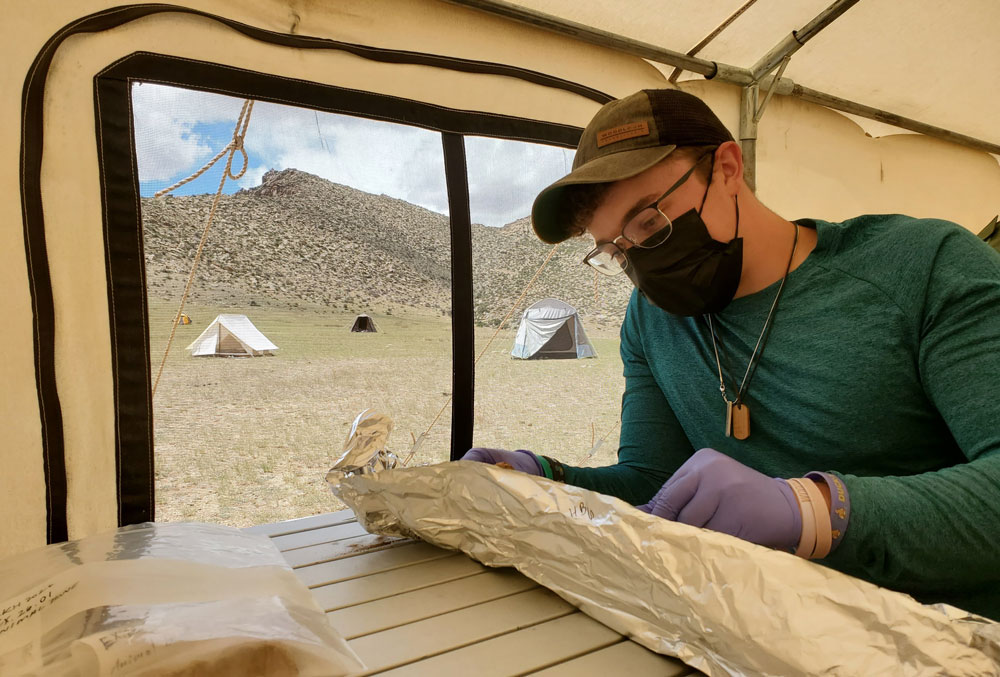 Eben Drake ’27 works with excavated artifacts and remains at a table inside a tent on the Mongolian steppe.