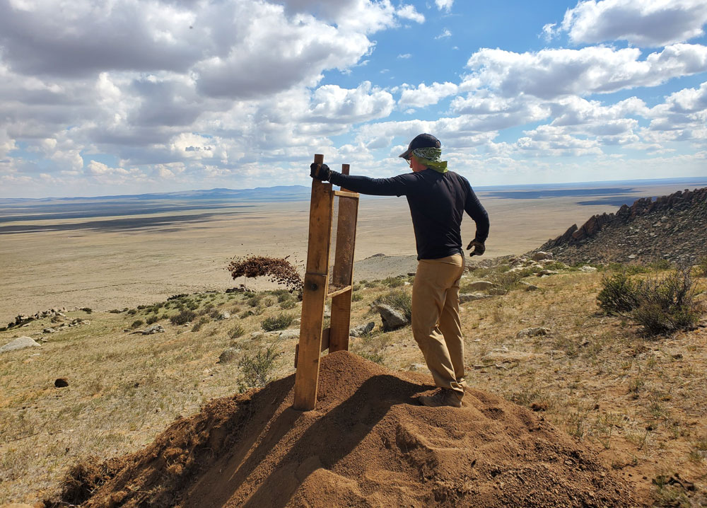 Eben Drake ’27 stands at an archaeological dig site on a Mongolian steppe, with his hand on a ladder